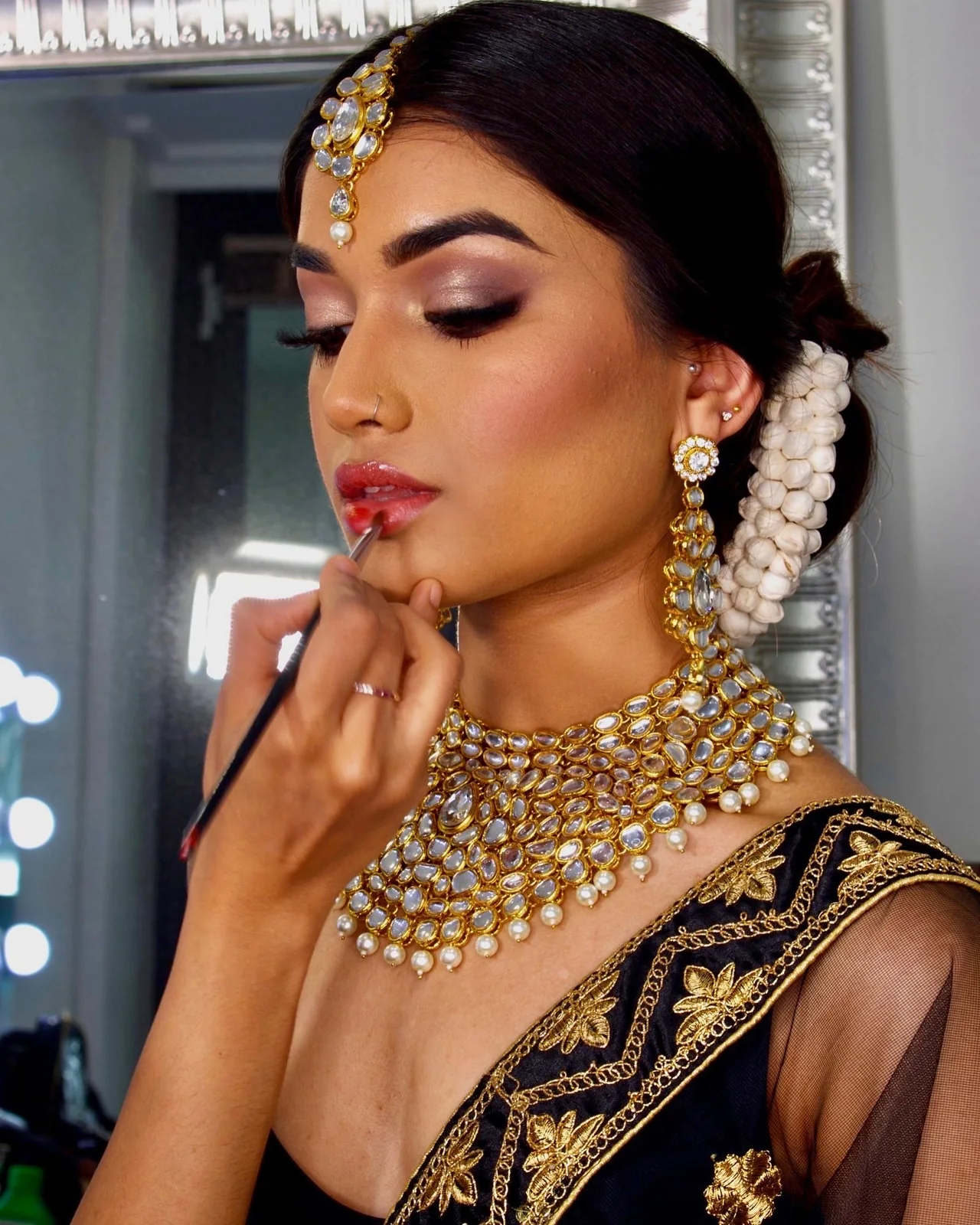 Bridal lip colour being refined beside gold jewellery and a jasmine-adorned updo