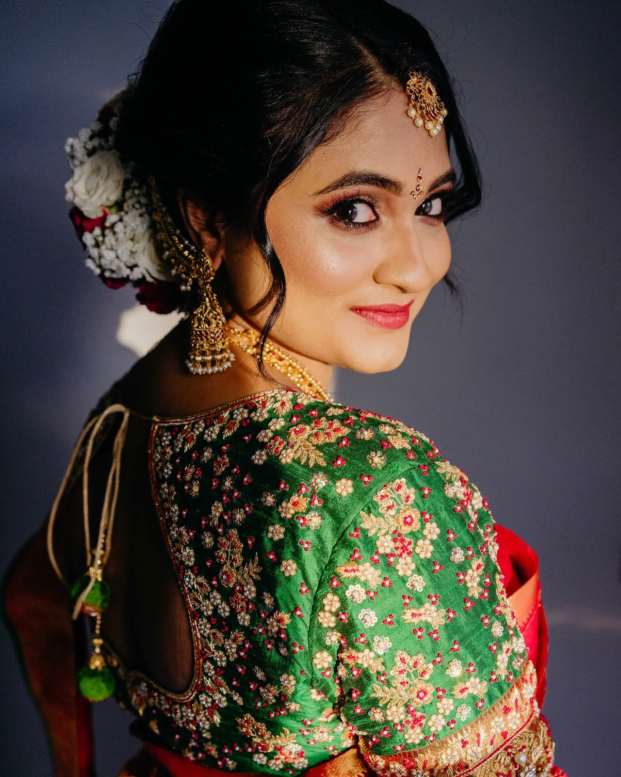 Bride looking over her shoulder in green and red silk, with a floral updo and defined eyes