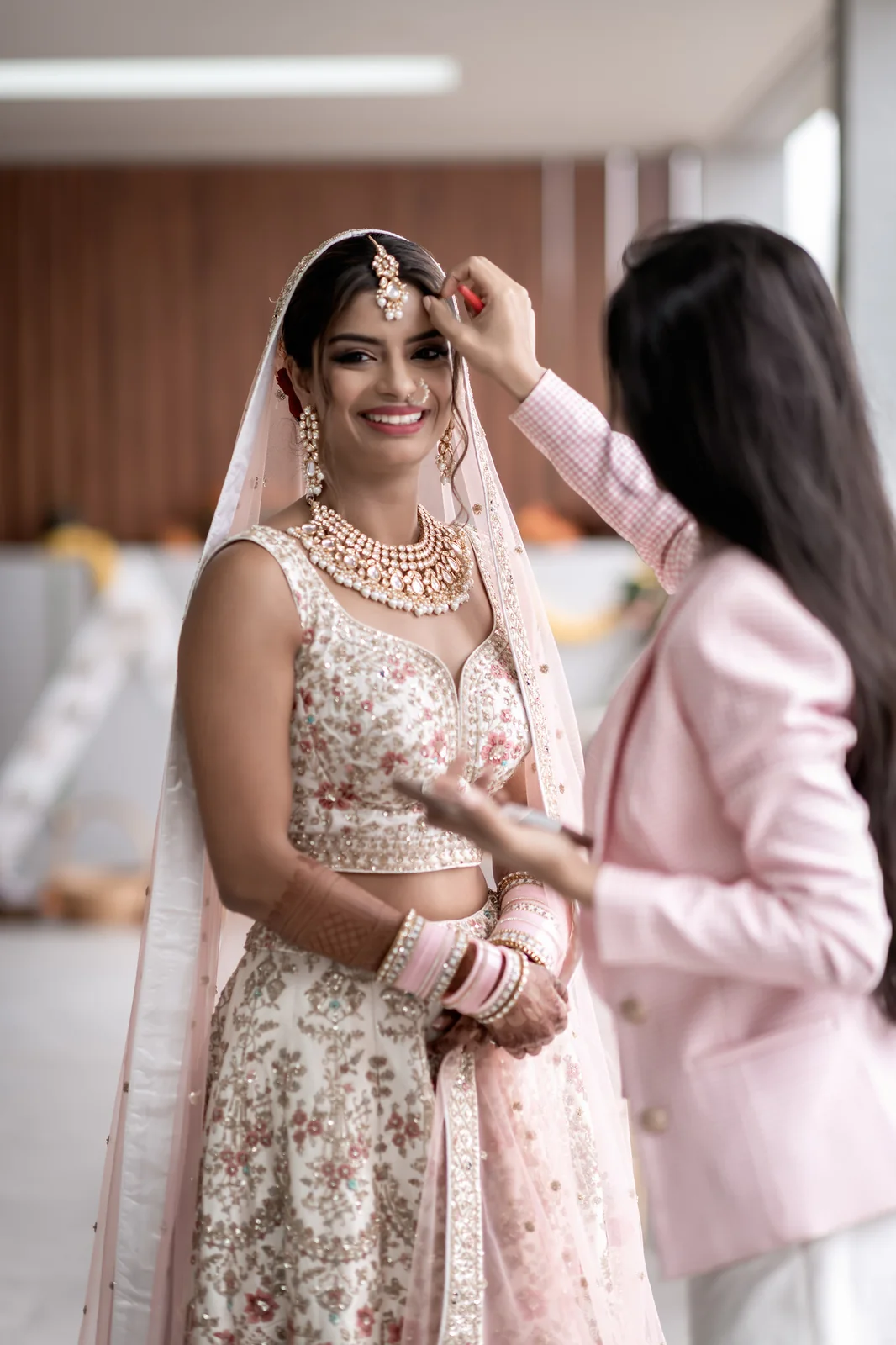 Heera refining the jewellery and hair framing of a smiling bride in pink