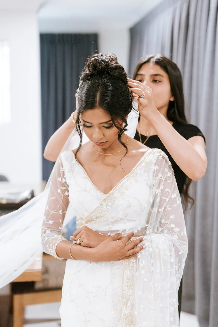 Heera refining an updo and placing the veil for a white-gown bride