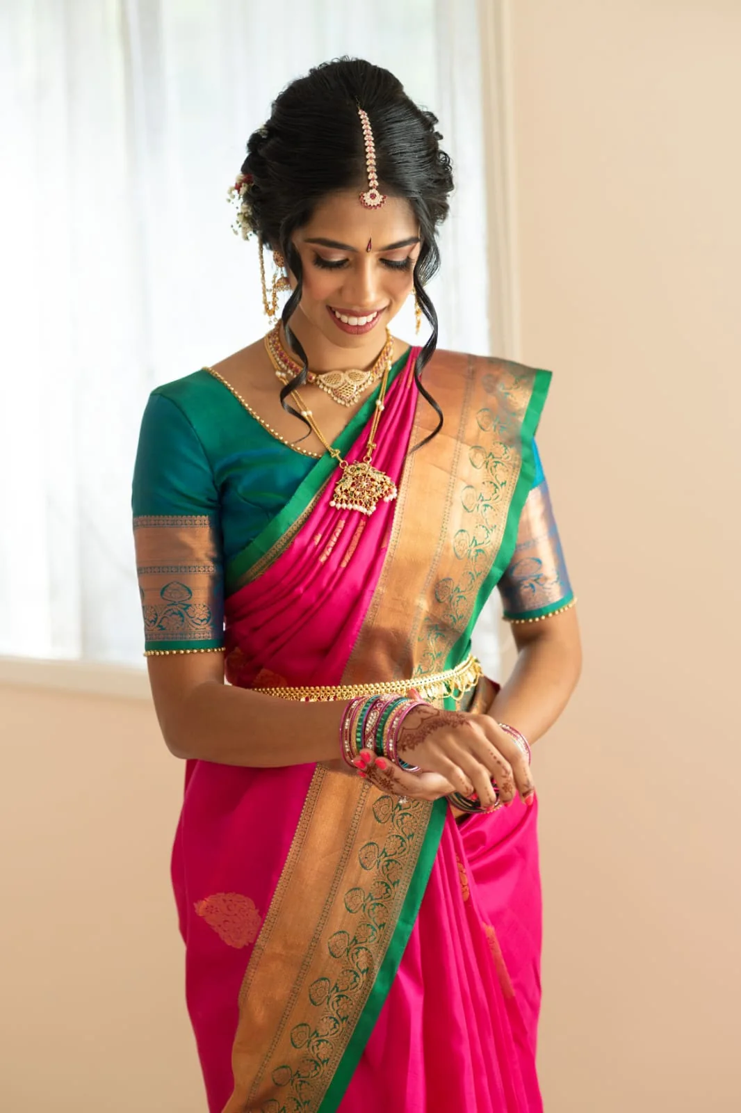 A pink and teal silk saree with gold jewellery and a softly framed updo