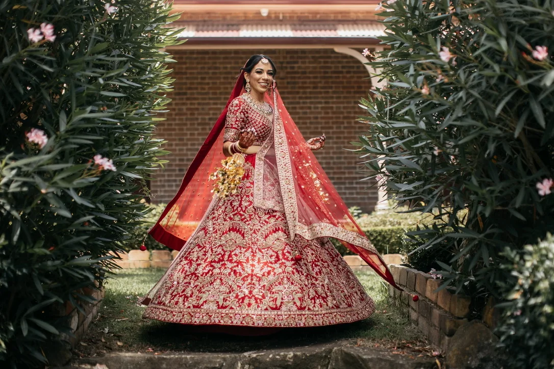 A red embroidered bridal outfit, veil and bouquet in a garden portrait