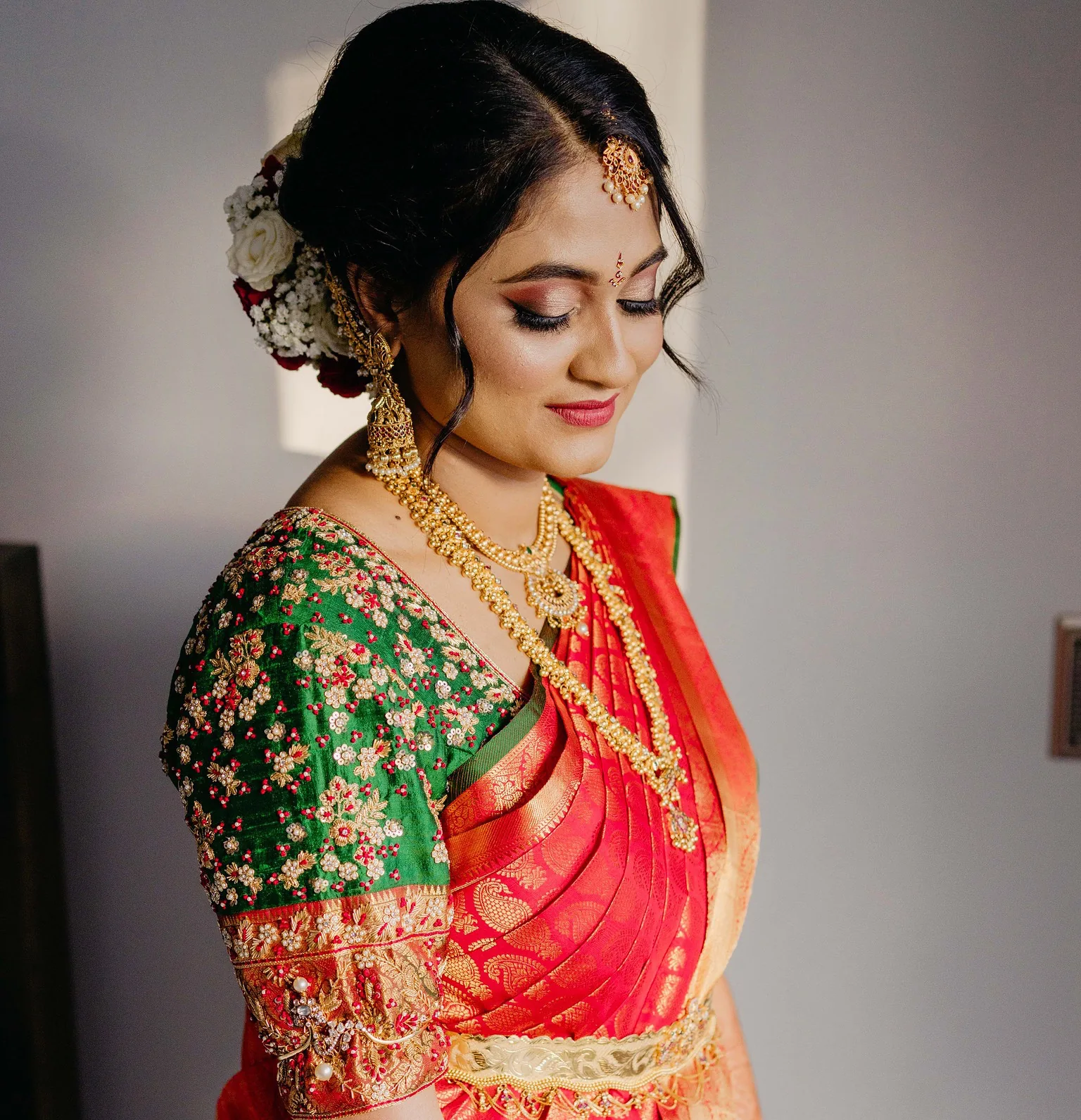 Bride in red and green silk with a floral updo, gold jewellery and softly defined bridal makeup