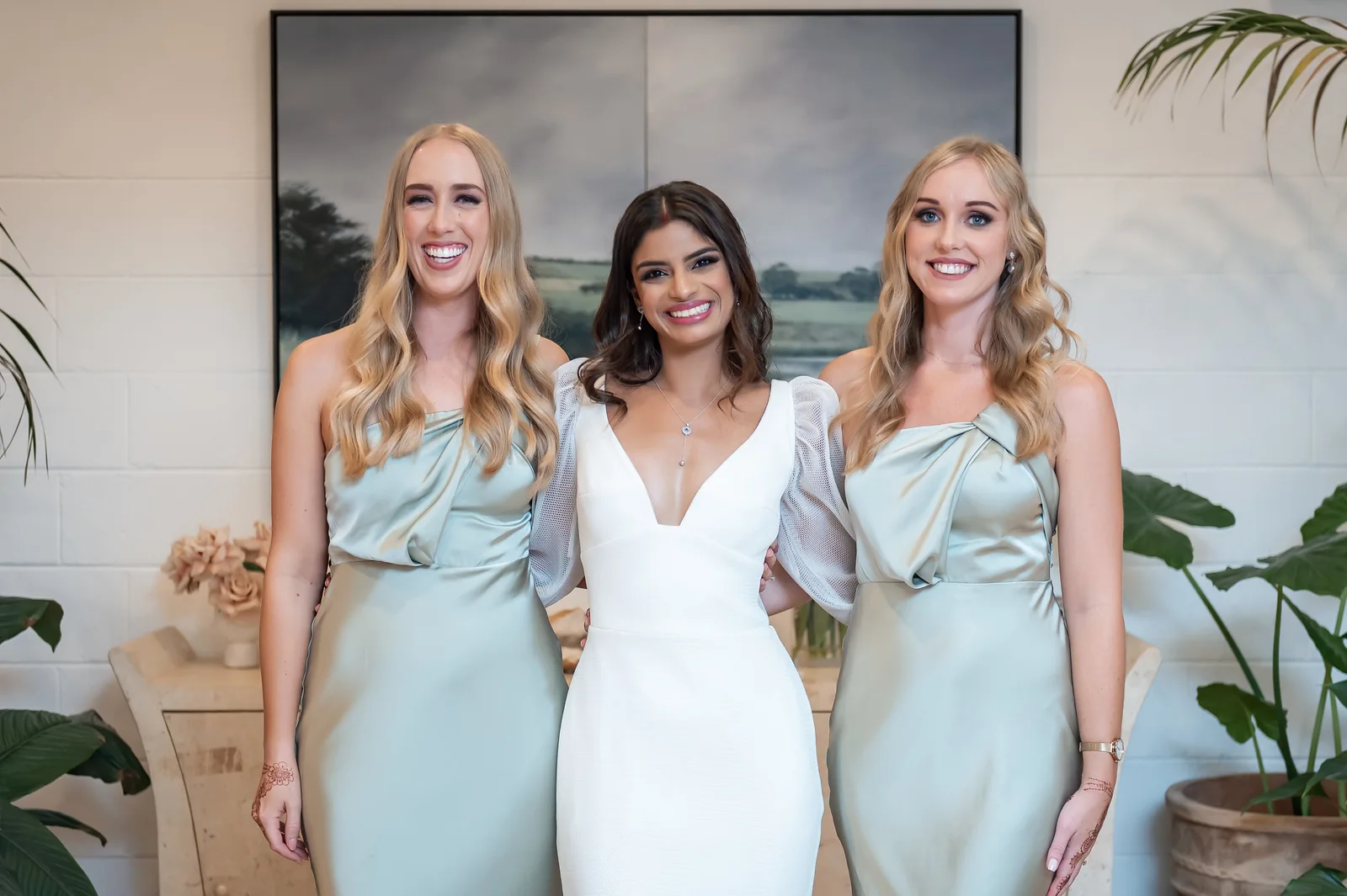 Shiv with softly waved hair and a white wedding gown, alongside two besties in pale blue