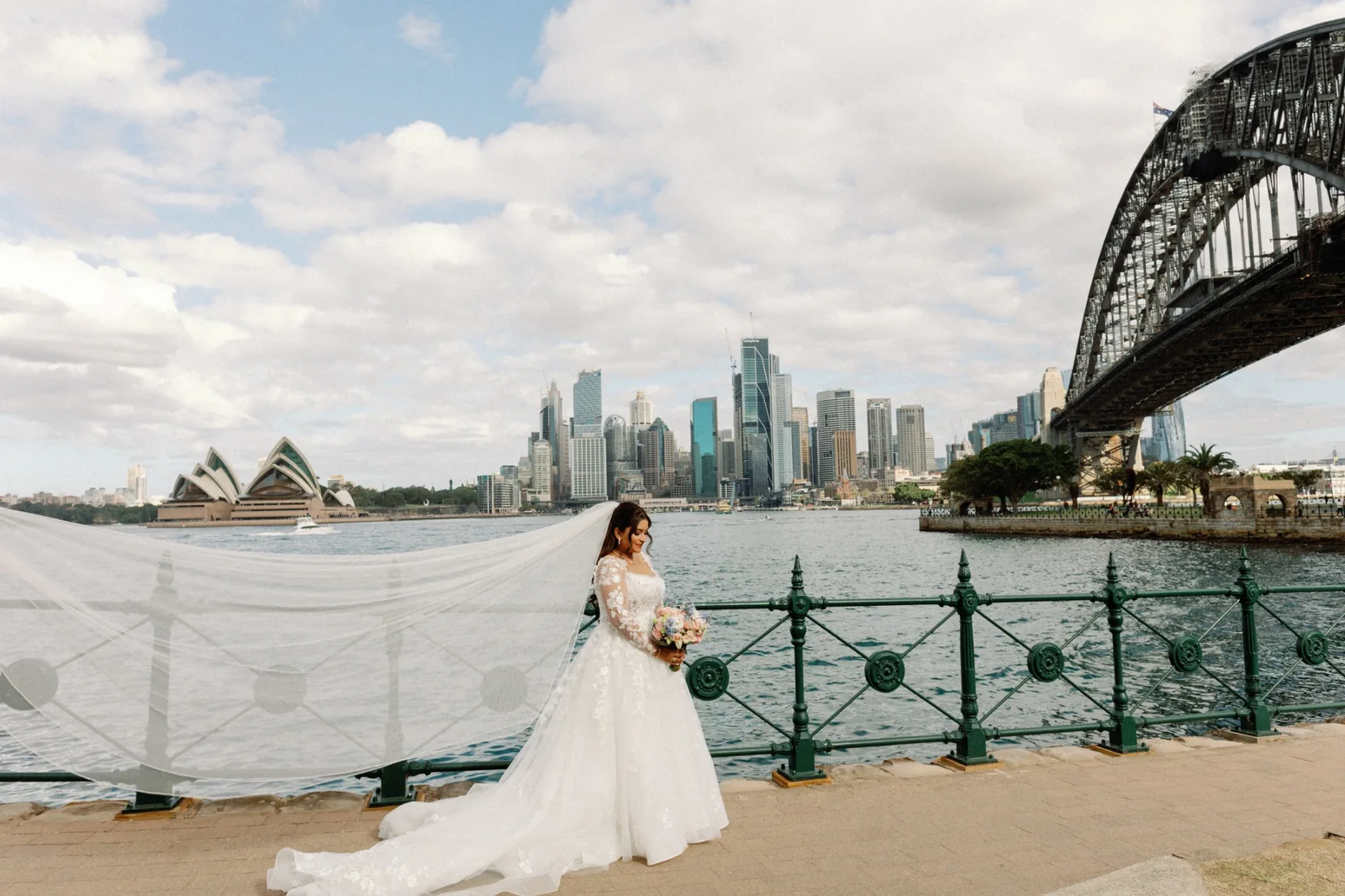 Bride in a white gown beside Sydney Harbour, the Harbour Bridge and Opera House