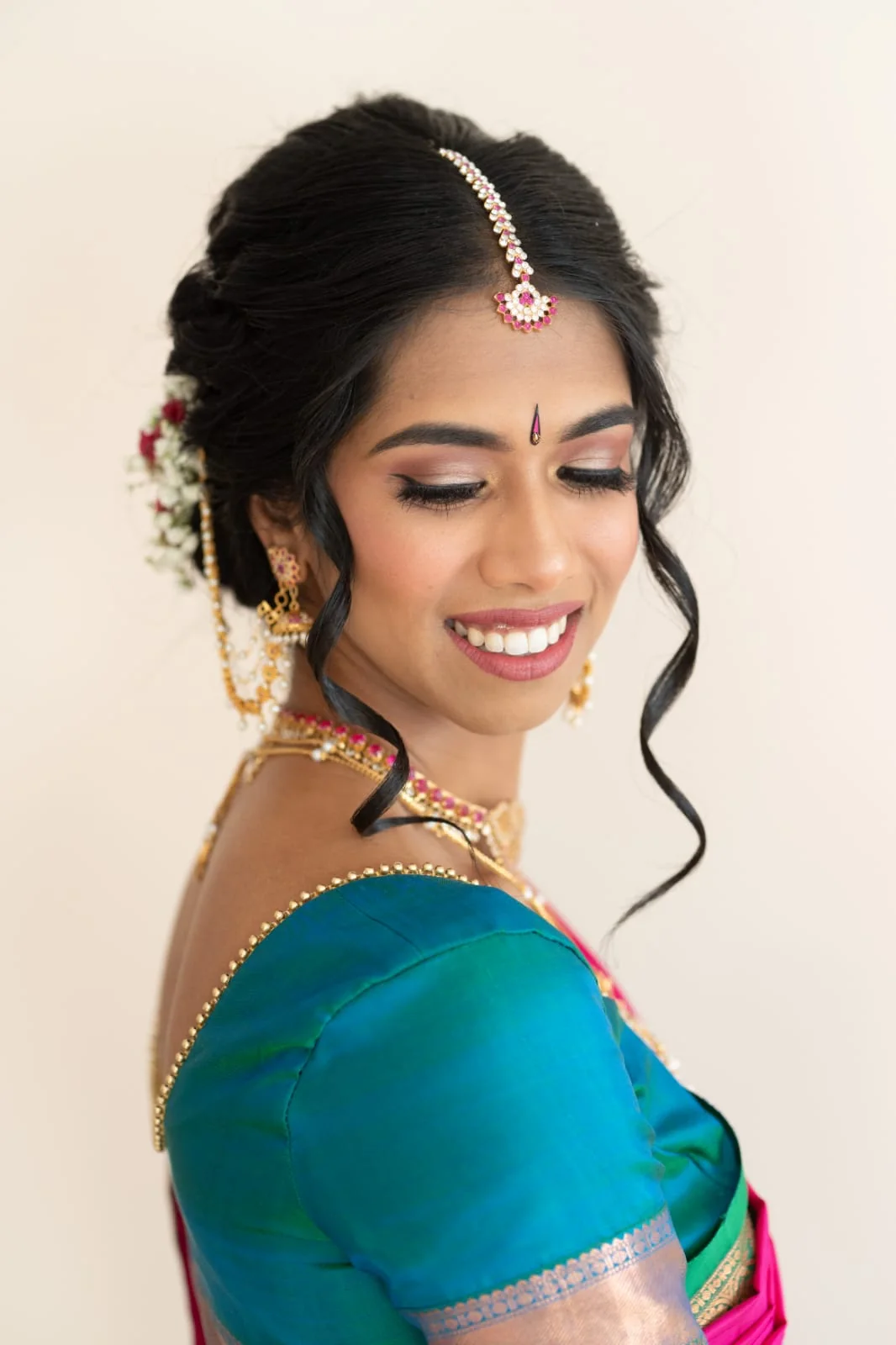 Smiling bride in teal silk with softly defined eyes, gold jewellery and a floral updo