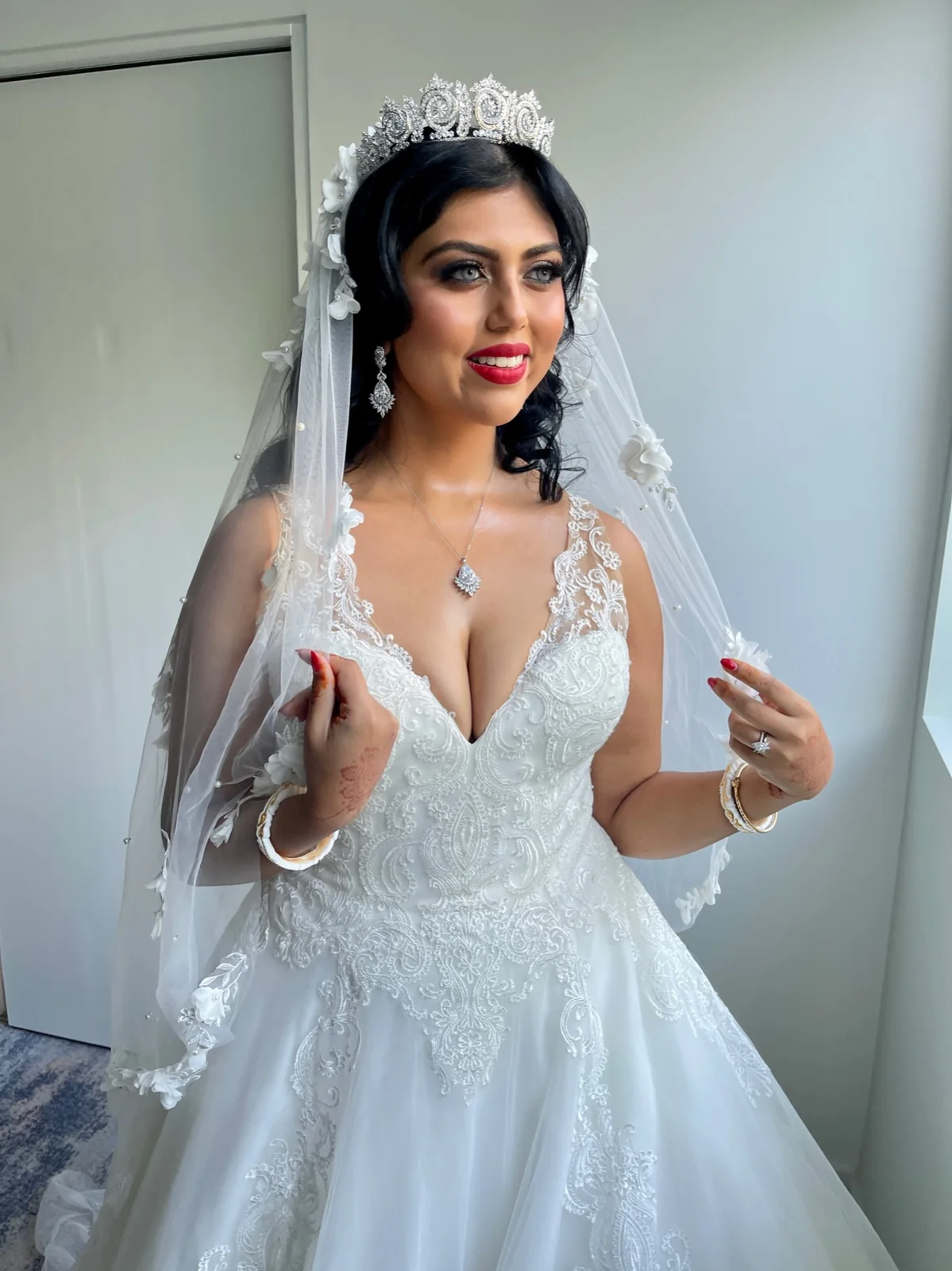 Bride in a white gown and veil with a tiara, softly framed hair and defined makeup