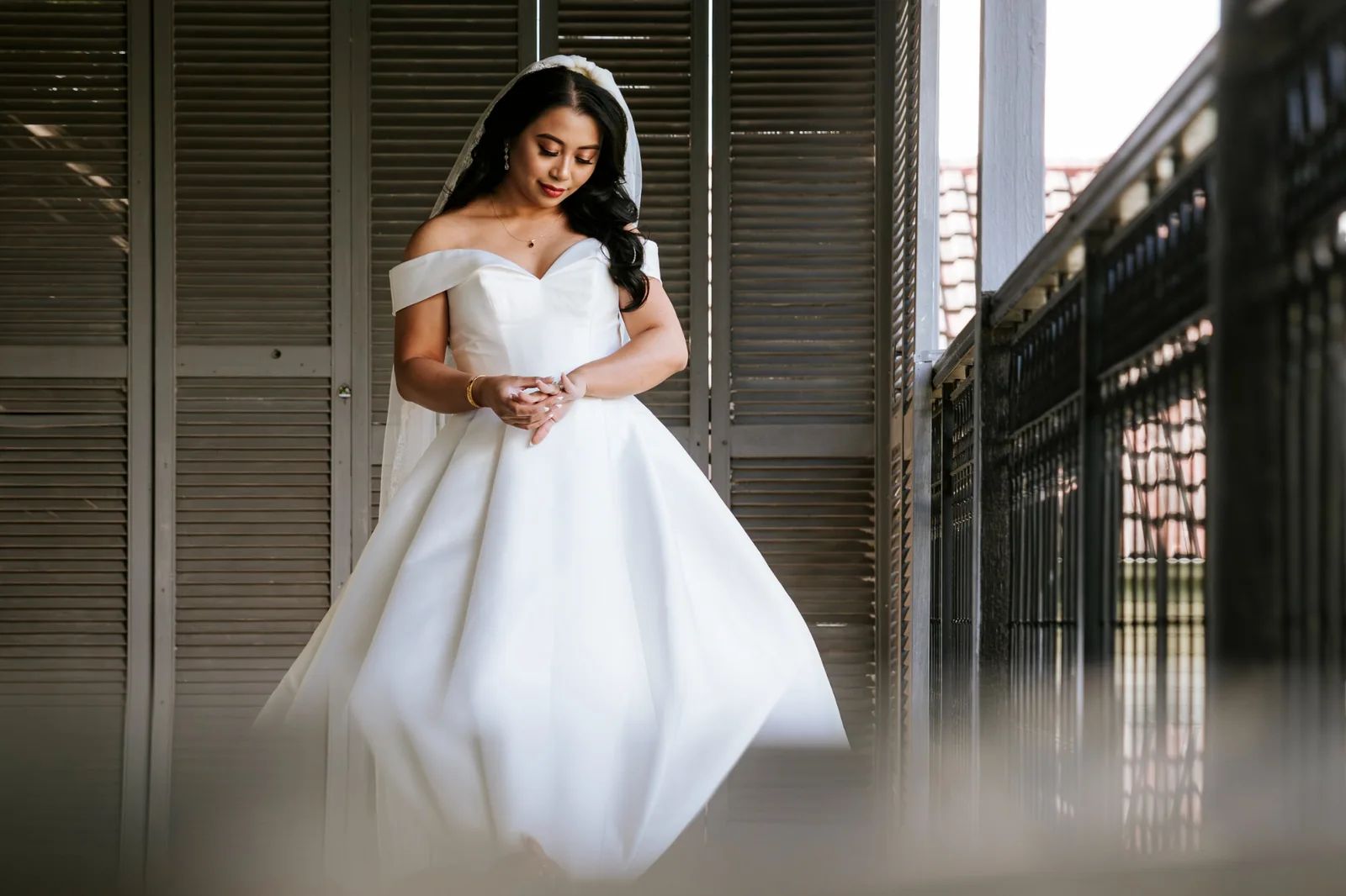 Bride with softly waved hair in a white gown beside tall windows