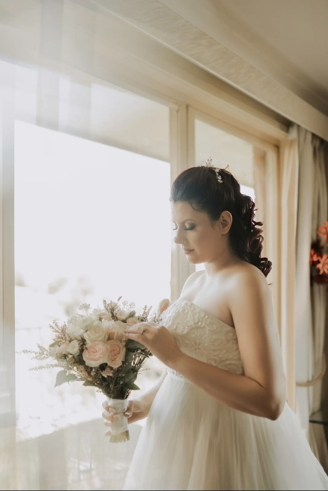 Heera’s softly styled white-gown bride holding her bouquet beside a window